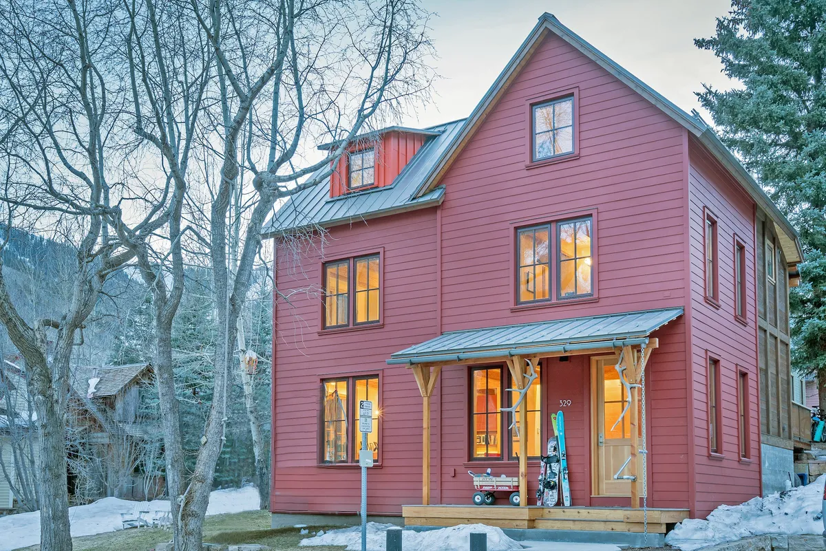 The welcoming red exterior of the home, complete with a wooden porch, large windows, and visible ski equipment. The scene suggests outdoor fun and easy access, appealing to families arriving for mountain getaways.
