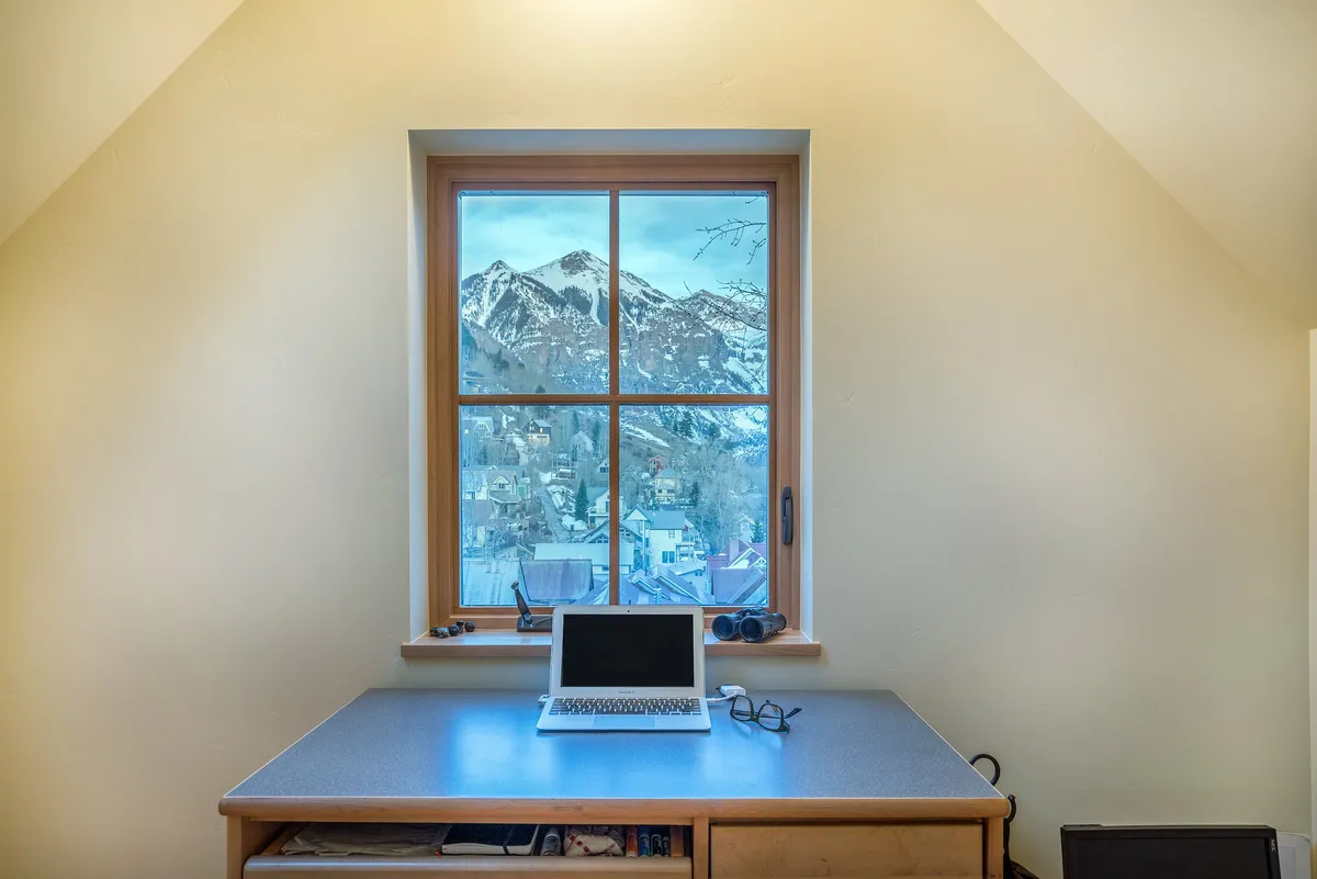 A compact study or flex space features a desk with a laptop, glasses, and a window framing inspiring mountain views. The setup is ideal for quiet work, creative pursuits, or an additional sleeping area if needed.
