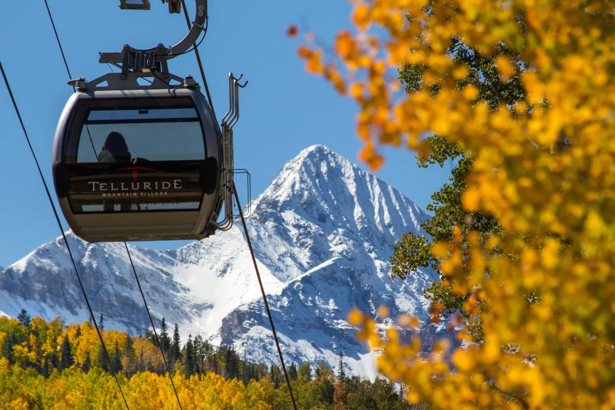 This image features the iconic Telluride gondola gliding above a landscape of snow-capped mountains and vibrant autumn foliage. The scene captures the seamless connection between the town and surrounding nature, and hints at year-round outdoor adventures accessible directly from the property.