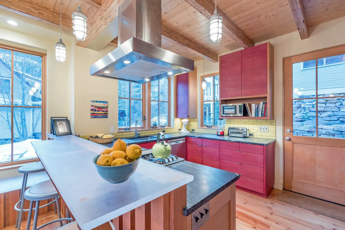 An interior shot featuring the kitchen island, vibrant artwork, large windows, and a well-equipped cooking range. Ample light fills the space, which is clearly designed for entertaining and family gatherings.